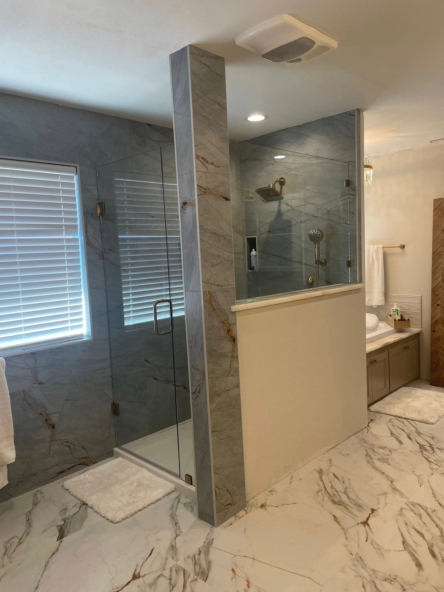 Modern bathroom featuring a glass shower, grey marble tiles, gold fixtures, and white marble floors.
