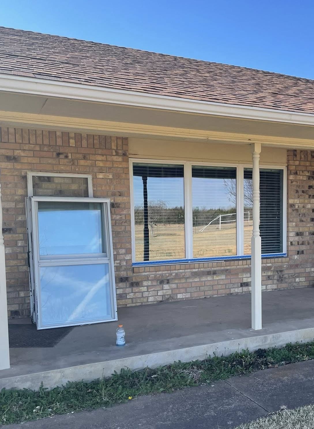 Large window installed on a brick house with old window frames leaning against the porch.